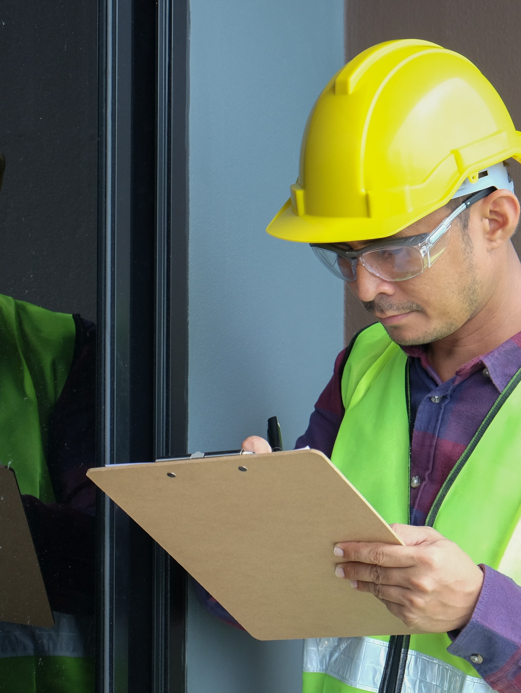 contractor in reflective vest and helmet reviewing a clipboard on a construction site.